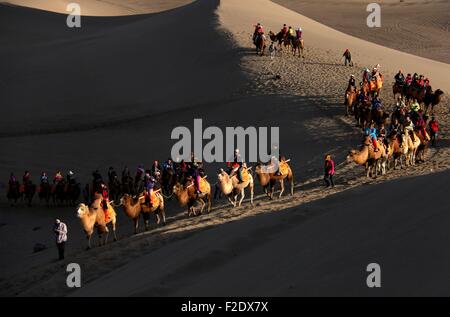 Jiuquan, Chinas Provinz Gansu. 16. Sep, 2015. Touristen fahren Kamele in den szenischen Bereich von crescent Frühling des Hügels berühmte in Dunhuang, Nordwesten Chinas Provinz Gansu, 16. September 2015. © Zhang Xiaoliang/Xinhua/Alamy Live-Nachrichten Stockfoto