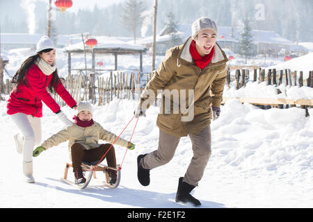 Glückliche Familie mit Schlitten im Schnee spielen Stockfoto