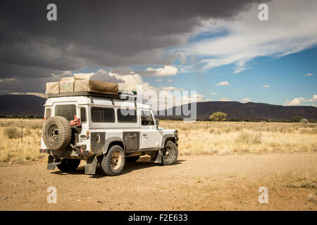 Land Rover Defender 110 geparkt mit Blick auf afrikanische Landschaft mit dunklen Wolken Overhead in Namibia, Afrika Stockfoto