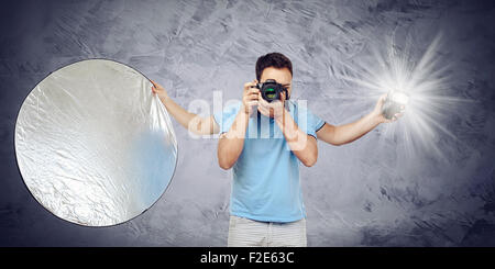 Fotograf mit vier Armen, die einen Blitz und Reflektor beim Fotografieren hält. Stockfoto