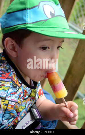 Ein kleiner Junge in eine grüne Baseballmütze isst ein Eis am Stiel. Stockfoto