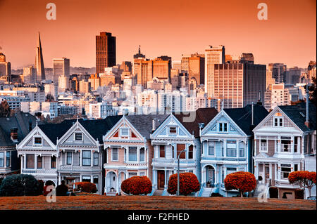 Reihe von farbenfrohen viktorianischen Häusern an der Steiner Street mit der Skyline von San Francisco hinter. Stockfoto