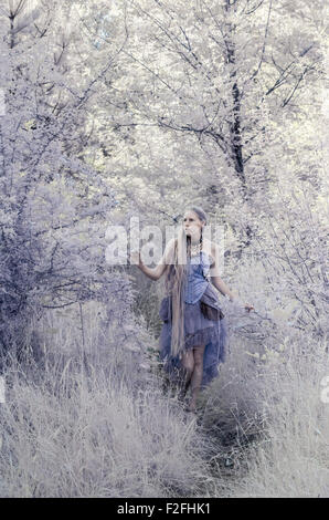 Eingefärbte Full Length Portrait of Young Woman Wearing lila Kleid auf Waldweg Wandern und erkunden bewaldeten Umgebung - Fair Stockfoto