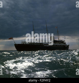 AJAXNETPHOTO. 1977. SOLENT, ENGLAND. -KÖNIGLICHE YACHT - DIE ROYAL YACHT BRITANNIA WEG UNTER GEWITTERHIMMEL KÖPFE FÜR COWES, ISLE OF WIGHT, UM ANKER AUS DEM HAFEN FÜR DIE COWES WOCHE SEGELN REGATTA FOTO: JONATHAN EASTLAND/AJAX REF: 703993 Stockfoto