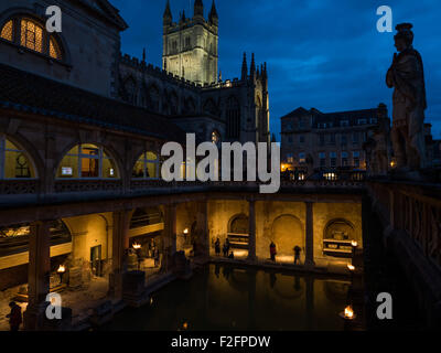 Eine Abend-Bild des berühmten römischen Bades in Bath am Abend mit Fackeln beleuchtet. Eine römische Statue steht auf der rechten Seite. Stockfoto