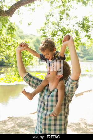 Verspielte Vater mit Sohn auf Schultern am Seeufer Stockfoto