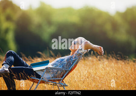 Unbeschwerte senior Frau mit Buch im sonnigen Bereich entspannen Stockfoto