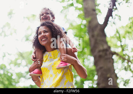 Lächelnde Mutter mit Sohn auf Schultern unter Baum Stockfoto