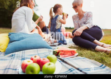 Äpfel und Wassermelonen auf Picknick-Decke in der Nähe von Multi-Generationen-Familie Stockfoto