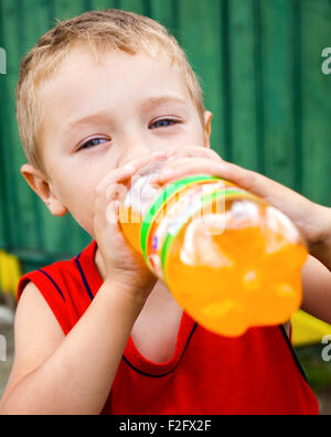 Durstige Kind trinken ungesund in Flaschen Orangenlimonade Stockfoto