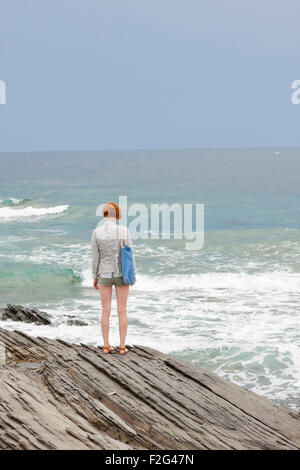 Mädchen mit roten Haaren steht am Rand der Klippe in Minorca Meer im Hintergrund Stockfoto