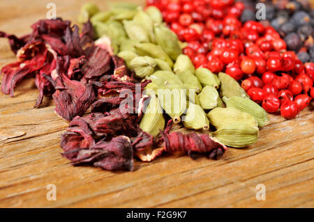 ein Haufen von getrockneten Hibiskusblüten, grüner Kardamom, rosa Pfefferkörner und Wacholderbeeren auf einem rustikalen Holztisch Stockfoto
