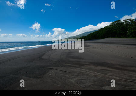 Küste Fischer Hütten in Nord-Sulawesi auf einem schwarzen Sandstrand mit tropischen üppigen im Hintergrund an einem sonnigen Tag mit blau Stockfoto