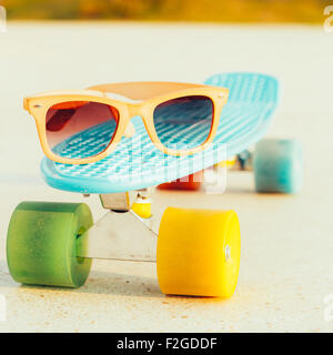 Sonnenbrille auf dem blauen Penny Board mit bunten Rädern steht auf der Spur Stockfoto