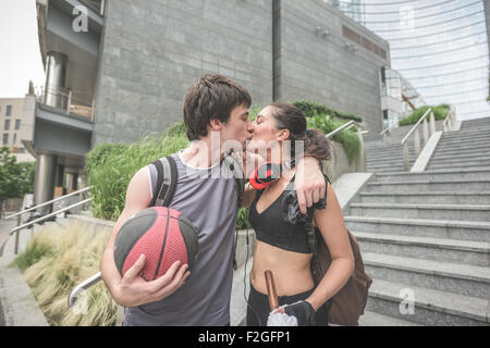 Paar schönen kaukasischen jungen sportlichen Mann und Frau zu Fuß nach unten, er ist ein Basketball in der Hand hält und küsst seine Freundin-entspannend, Break, sportliches Konzept Stockfoto