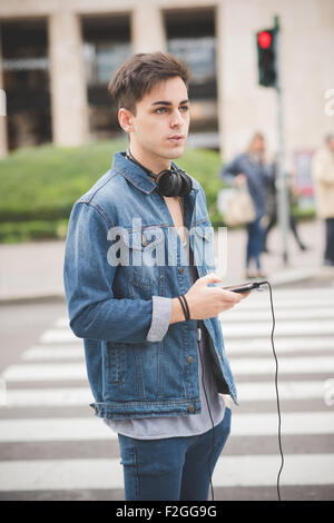 Knie-Figur des schönen jungen alternative Mann mit zentralen Labret und Nasenloch Piercings in der Stadt Musikhören mit Kopfhörer und Smartphone verbunden Wireless - Technologie, Kommunikations-Konzept Stockfoto