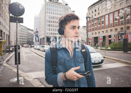 halbe Länge des schönen jungen alternative Mann mit zentralen Labret und Nasenloch piercing Musikhören mit Kopfhörer und Smartphone verbunden Wireless - Technologie, Kommunikation, Musikkonzept Stockfoto