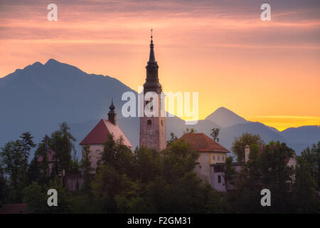 Katholische Kirche in Bled See, Slowenien bei Sonnenaufgang mit den Bergen im Hintergrund Stockfoto