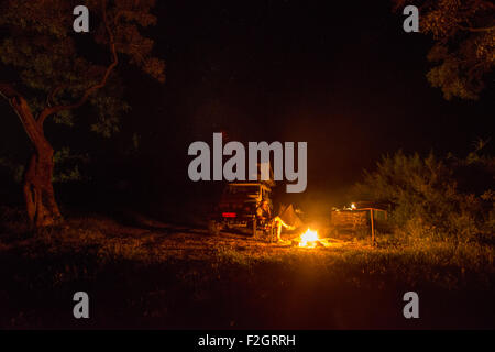 Mann sitzt durch einen Brand am Telefon mit seinem Land Rover im Hintergrund in Botswana, Afrika Stockfoto