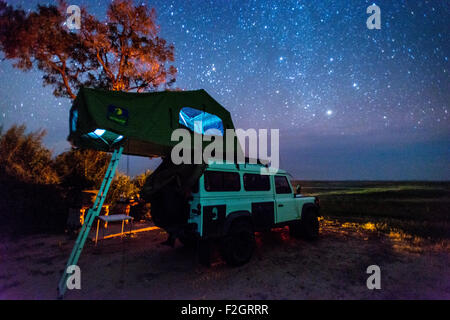 Land Rover geparkt mit einem Pop-up-Zelt auf dem Dach unter dem Nachthimmel in Botswana, Afrika Stockfoto