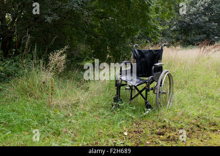 Rollstuhl sitzt in einem bewachsenen Feld verlassen. Stockfoto