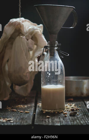 Retro-Glasflasche milchfreien Mandelmilch mit alten Trichter, gemahlenen Mandeln und Vintage Geschirr im Hintergrund. Dunkle rustikale st Stockfoto