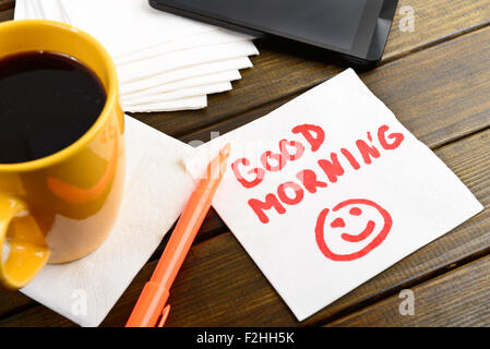 Guten Morgen schreiben auf weiße Serviette rund um Kaffee Stift und Telefon auf Holztisch