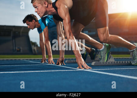 Zwei junge Sportler in Ausgangsposition bereit, ein Rennen zu starten. Sprinter bereit für Rennen auf der Rennstrecke mit Sonne Flare. Stockfoto