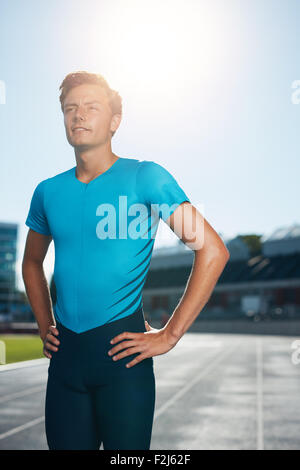 Professionelle Mann Sportler mit seinen Händen auf den Hüften, Blick in die Ferne hinter der Kamera stehen. Sprinter steht in der Spur zu den am Stockfoto