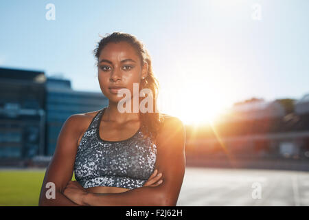 Porträt von überzeugt junge Sportlerin stehend mit den Händen auf Leichtathletik-Stadion Blick in die Kamera mit hellen Sunlig gefaltet Stockfoto