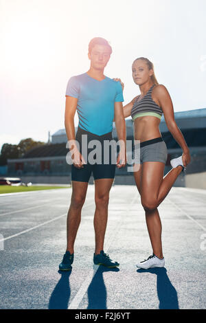 Voller Länge Schuss der junge Mann und Frau stehen auf Leichtathletik Rennen verfolgen, an einem sonnigen Tag. Athleten auf der Laufstrecke St passen Stockfoto