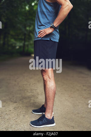 Kopflose Schuss von einem athletischen jungen Mann in Seitenansicht, stehen im Park mit Hand auf Taille. Stockfoto