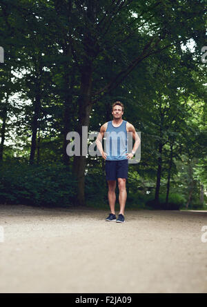 Sportliche junge Mann stehen im Park mit Händen hält seine Taille und suchen in der Ferne. Stockfoto