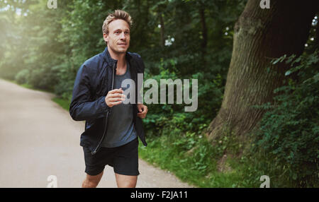 Drei Viertel Schuss eines gesunden jungen Mannes in Jacke Hemd, Joggen im Park in den frühen Morgenstunden. Stockfoto