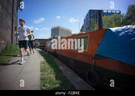 Läufer und Jogger auf dem Treidelpfad, vorbei an einem Kanalboot vor Anker auf dem Treidelpfad des Regent es Canal in der Nähe von Kings Cross in London Stockfoto