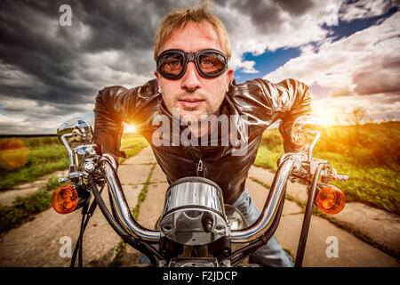 Biker Mann trägt eine Lederjacke und eine Sonnenbrille sitzt auf seinem Motorrad, Blick auf den Sonnenuntergang, Rennen auf der Straße. Filter-ap Stockfoto