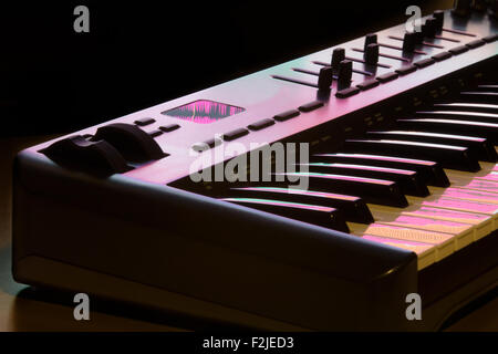 Deatil von einem MIDI-Keyboard mit Modulationsrad, beleuchtet von einem Computer-Bildschirm. Eine Wellenform spiegelt sich auf dem Display. Stockfoto