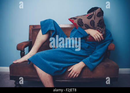 Junger Mann im Bademantel auf dem Sofa sitzen Stockfoto
