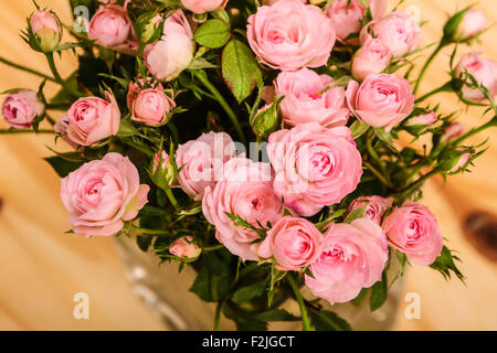 Haufen von kleinen rosa Rosen in einer Glasvase auf einem Holztisch. Stockfoto