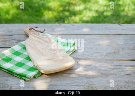 Leer aus Holz Gartentisch mit Schneidbrett über Tischdecke mit grünen sonnigen Bokeh Hintergrund Stockfoto