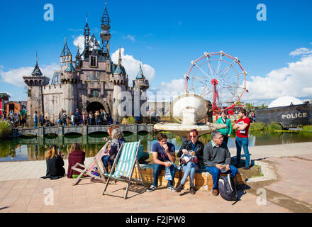 Menschen genießen die Ironie von Banksy Dismaland mit Märchenschloss und Riesenrad und Polizei Riot Brunnen Weston Super Mare UK Stockfoto