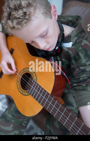 Blonde kaukasischer junge 11 Jahre alt, üben die Akkustik Gitarre tragen beats Kopfhörer Stockfoto