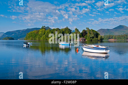 Blick auf kleine Boote vor Anker am Derwentwater bewaldeten Derwent Insel, steigt hinter Fjälls, ruhigen sonnigen Morgen, Cumbria UK Stockfoto