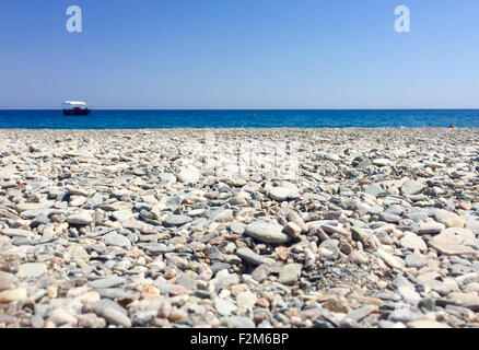 Detail aus Steinen und Sand in einem einsamen Strand mit Meer und ein Boot im Hintergrund Stockfoto