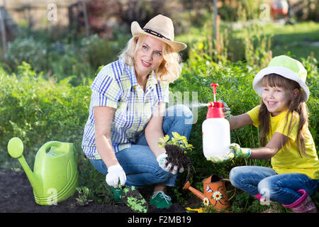 Glückliche Frau und Kind Mädchen auf Bauerngarten im Sommer, Erdbeeren zu Pflanzen. Glückliche Familie Zeit miteinander zu verbringen. Mutter des Kindes helfen. Stockfoto