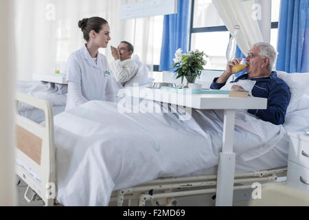 Krankenschwester sucht bei älteren Patienten im Krankenhausbett Stockfoto