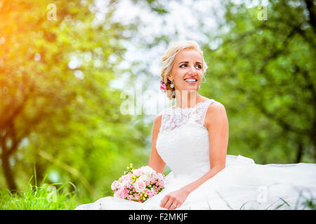 Schöne junge Braut im Hochzeitskleid sitzen in der Wiese Stockfoto