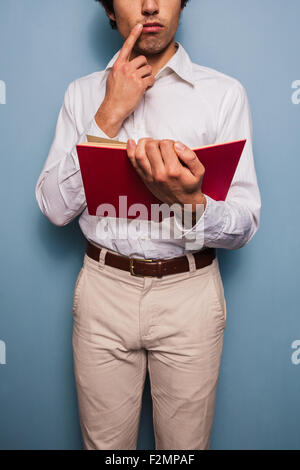 Junger Mann stehend mit einer blauen Wand Buch Stockfoto