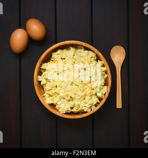 Frische hausgemachte Eisalat mit Mayonnaise und Senf in Holzschale Holzlöffel auf der Seite mit rohen Eiern zubereitet Stockfoto