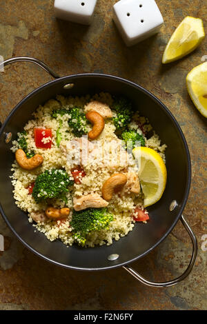 Couscous-Gericht mit Huhn, Broccoli, Tomaten, Cashew-Nüssen. Zitrone, Salz- und Pfefferstreuer auf der Seite Stockfoto